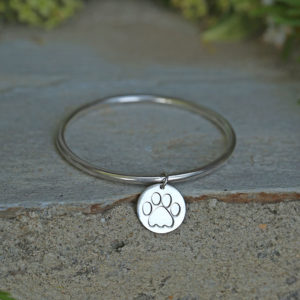 A child's silver bangle with a round charm with paw.