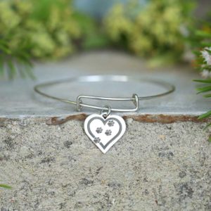 A silver bangle with a heart engraved with paws.