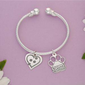 A silver torque lined bangle with a heart with paws engraved and Paw with name charms